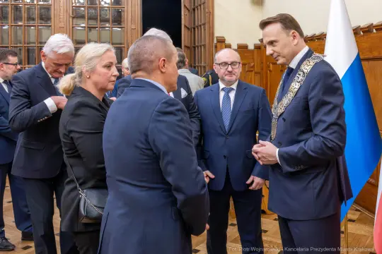 Spotkanie osób w eleganckich strojach, rozmowa przy flagach.