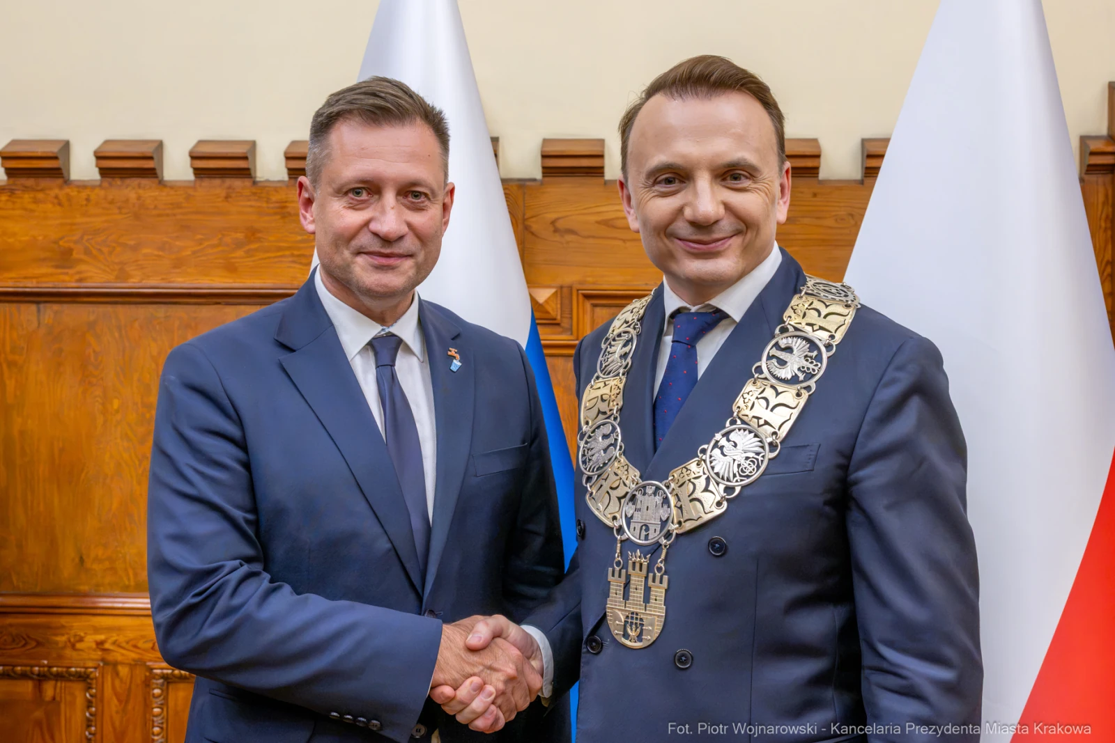 Dwaj mężczyźni w garniturach uścisnęli sobie dłonie, w tle flagi.  Autor: Piotr Wojnarowski