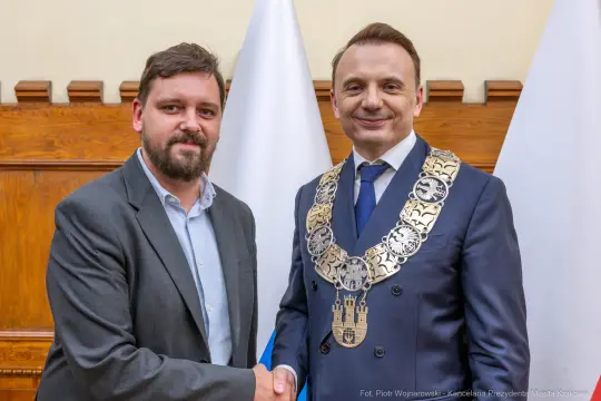 Mężczyźni w garniturach uścisną ręce, jeden z łańcuchem prezydenckim.