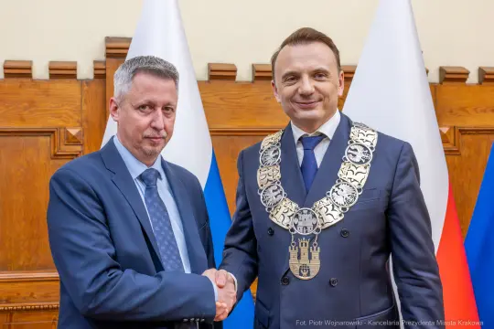 Dwaj mężczyźni w garniturach, jeden z łańcuchem prezydenckim, uściski dłoni.
