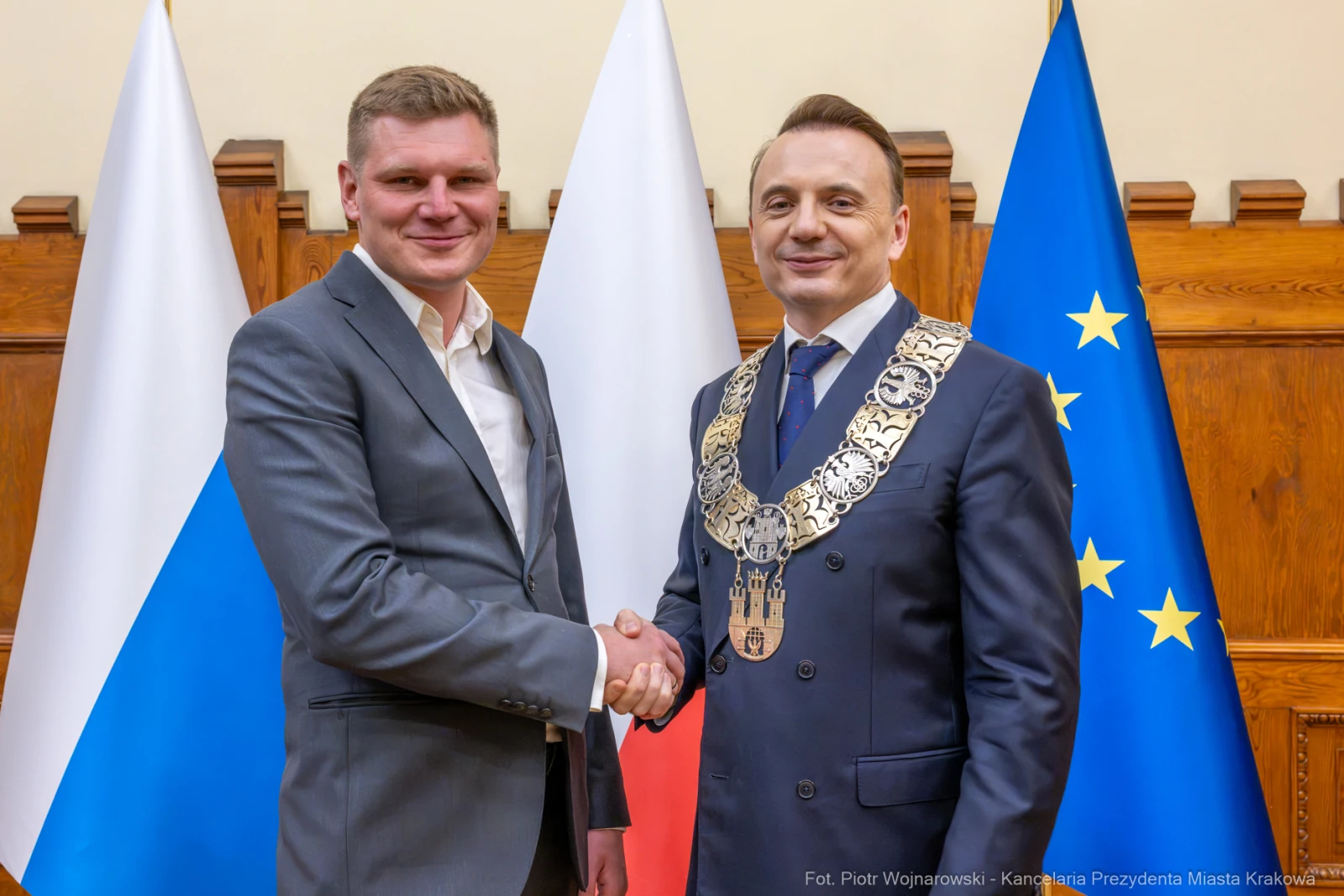 Dwaj mężczyźni w garniturach uścisnęli sobie dłonie, w tle flagi Polski i Unii Europejskiej.  Autor: Piotr Wojnarowski