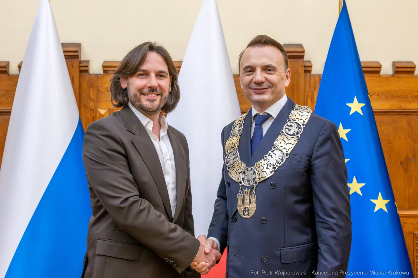 Mężczyźni w garniturach uścisną ręce, w tle flagi Polski i Unii Europejskiej.  Autor: Piotr Wojnarowski