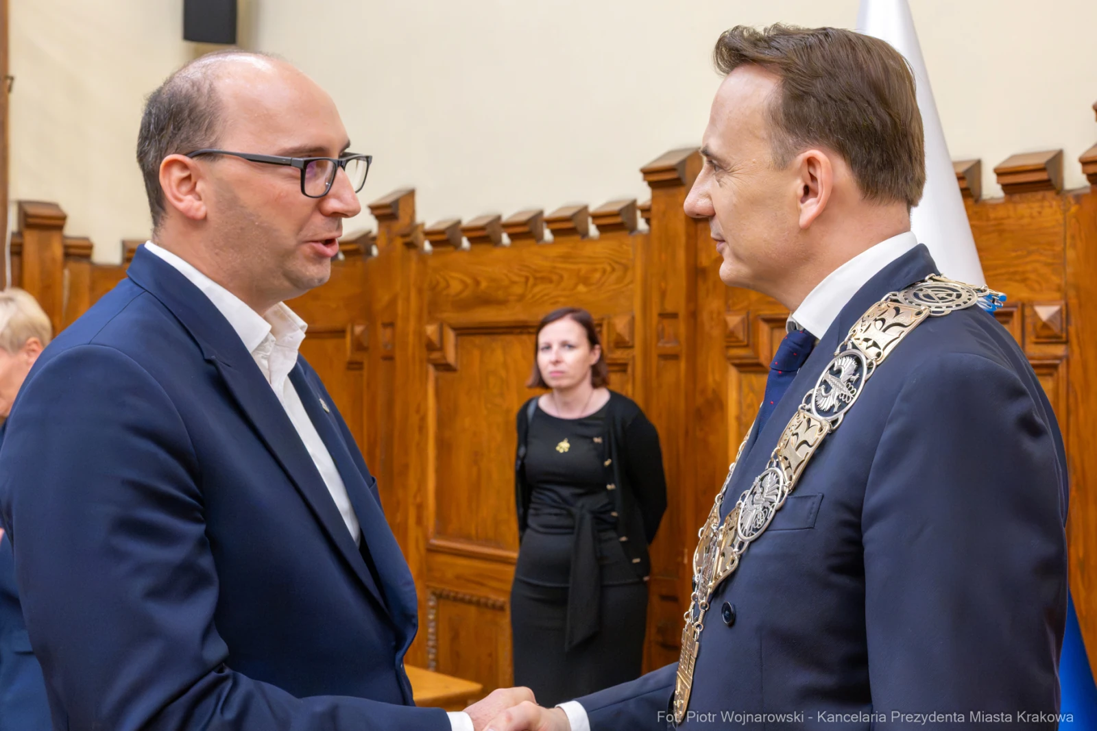 Dwaj mężczyźni uścisnęli sobie dłonie w formalnej atmosferze. W tle kobieta w czerni.  Autor: Piotr Wojnarowski