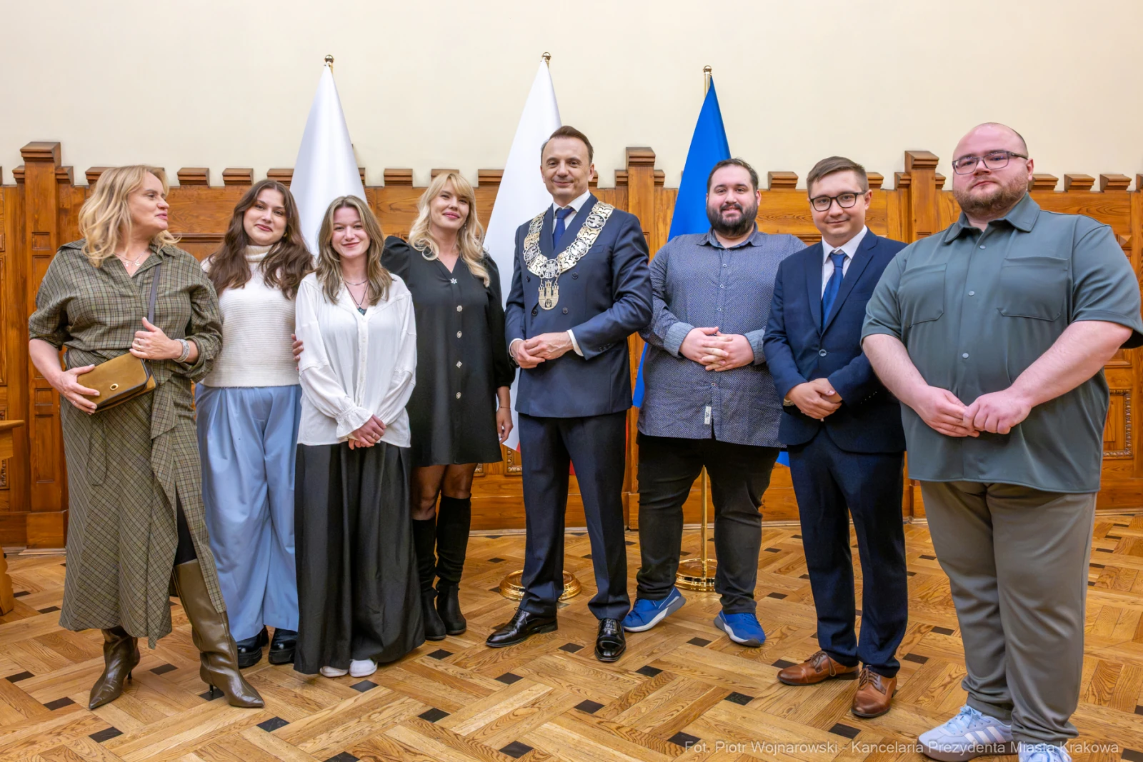 Grupa osób w formalnych strojach, w tym mężczyzna w łańcuchu, na tle flag.  Autor: Piotr Wojnarowski