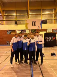 Grupa sportowców w strojach reprezentacyjnych trzymająca transparent w hali sportowej.