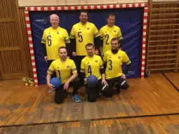 Grupa sześciu mężczyzn w żółtych koszulkach sportowych, trzymających niebieskie piłki.