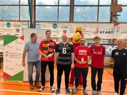 Uczestnicy turnieju sportowego z nagrodami, w tym maskotka i przedstawiciele organizacji.