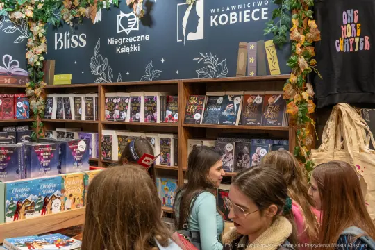 Książki na półkach w wydawnictwie, osoby przeglądające ofertę.