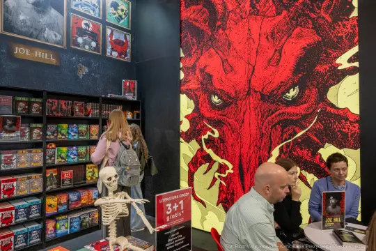 Stoisko z książkami Joe Hilla, z czerwonym muralem i dekoracjami w stylu horroru.