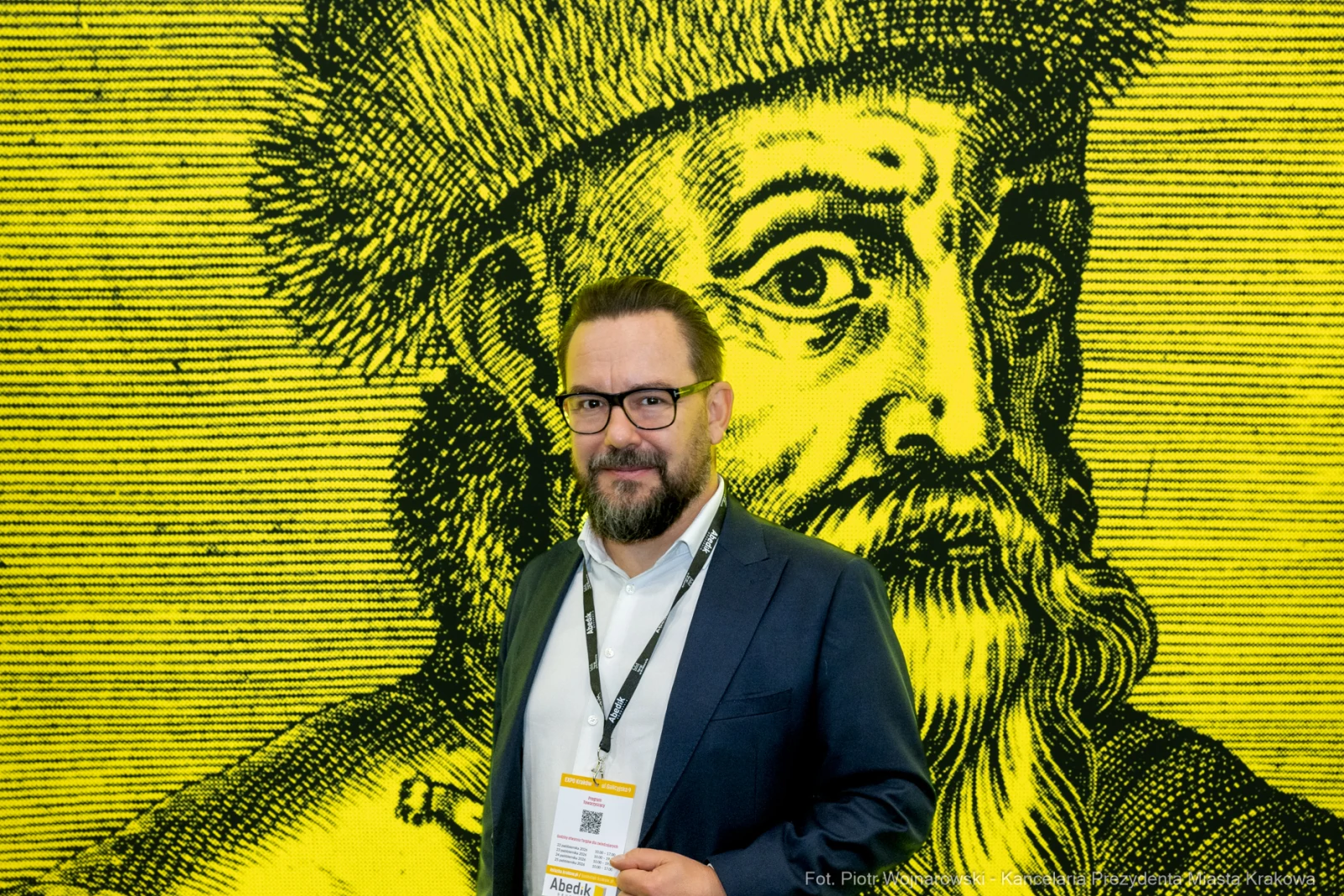 Mężczyzna w okularach stoi przed żółtą grafiką z wizerunkiem historycznej postaci.  Autor: Piotr Wojnarowski
