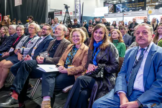 Grupa ludzi siedzących na widowni podczas wydarzenia, uśmiechnięci i zaangażowani.