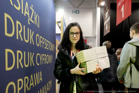 Kobieta trzyma stos książek w tle z grafiką promującą usługi druku.