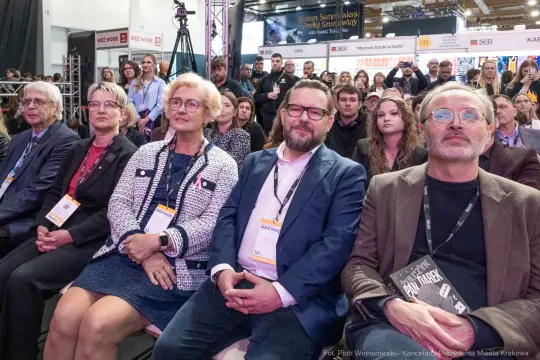Grupa ludzi siedzących na wydarzeniu, z zainteresowaniem słuchających prelekcji.
