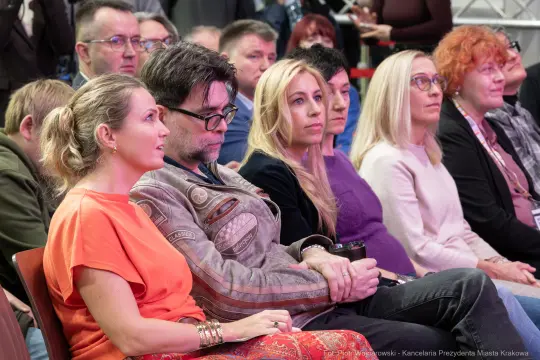 Grupa ludzi siedzących na wydarzeniu, skupionych na prelekcji.