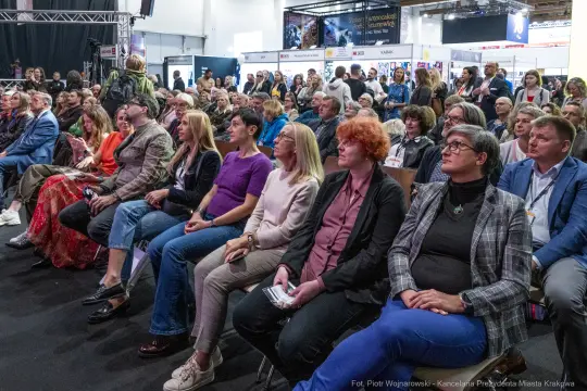 Tłum ludzi siedzących na wydarzeniu, skupionych na prelekcji lub prezentacji.