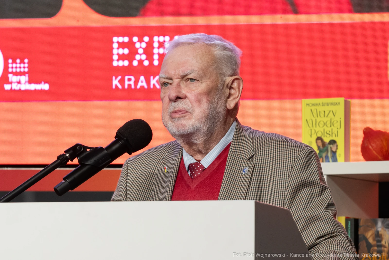 Mężczyzna w garniturze przemawia do mikrofonu na tle kolorowych plansz.  Autor: Piotr Wojnarowski