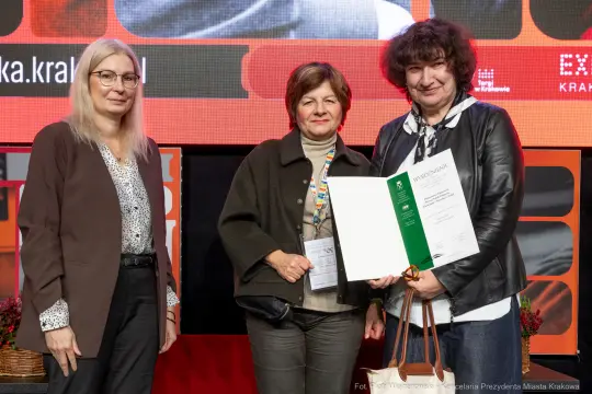 Trzy kobiety na scenie z dyplomem i nagrodą.