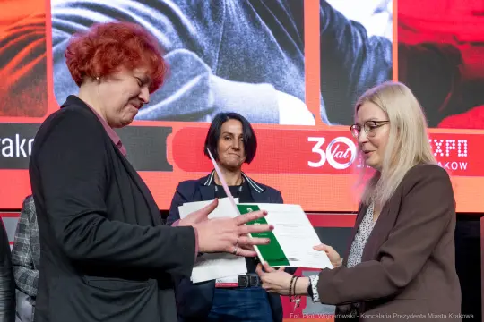 Wręczenie dokumentów podczas wydarzenia, trzy kobiety w formalnych strojach.
