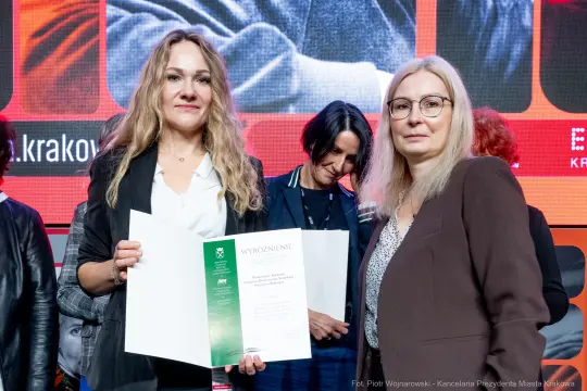 Dwie kobiety trzymają dyplom, w tle inni uczestnicy wydarzenia.