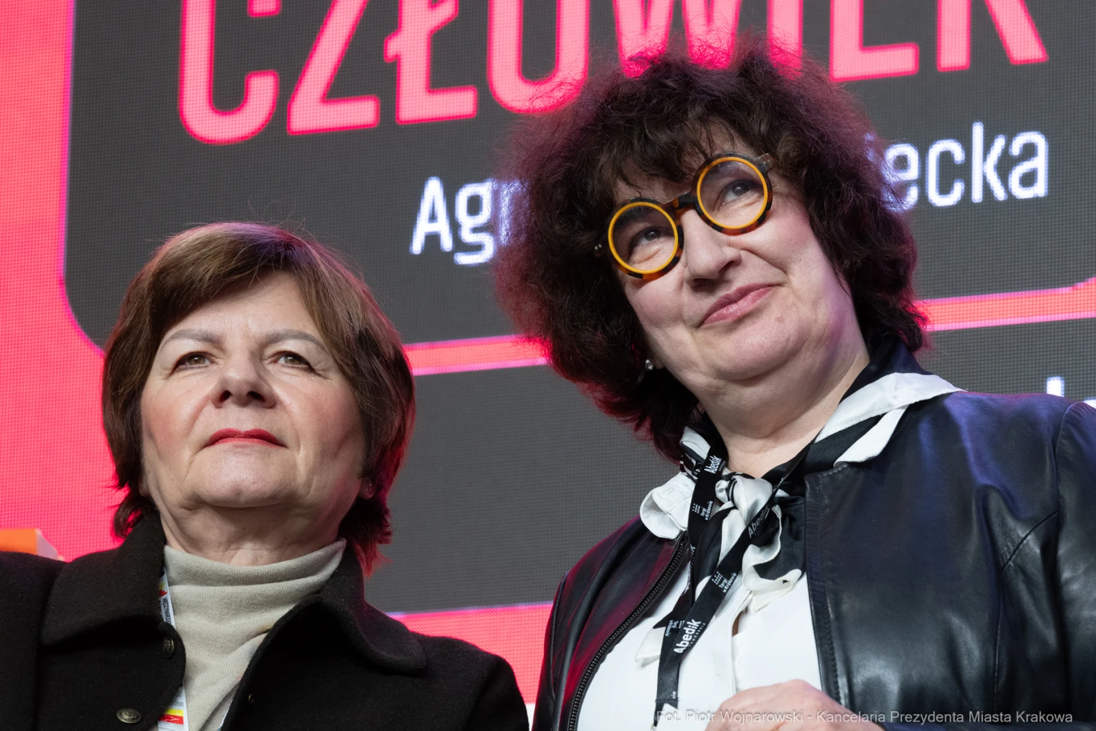 Dwie kobiety z okularami, uśmiechające się na tle kolorowego tła z napisem.  Autor: Piotr Wojnarowski
