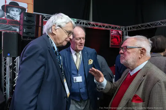 Trzech mężczyzn rozmawia w towarzystwie sprzętu audio i wystawienniczego.