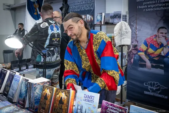 Mężczyzna w kolorowym stroju przegląda książki na stoisku podczas wydarzenia.