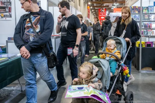 Tłum ludzi w strefie wystawowej, dzieci w wózku przeglądające książki.