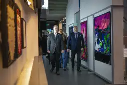 Mężczyźni w garniturach spacerują w galerii sztuki obok kolorowych obrazów.