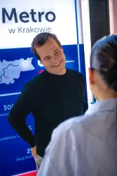 Mężczyzna rozmawia z kobietą w tle z grafiką dotyczącą metra w Krakowie.