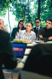 Grupa ludzi słuchających prezentacji, na stole jedzenie i napoje.