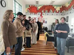 Grupa ludzi słuchająca prezentacji w pomieszczeniu z muralem smoka.