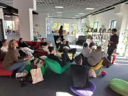 Grupa ludzi w kolorowych fotelach, rozmawiających w nowoczesnej przestrzeni biurowej.