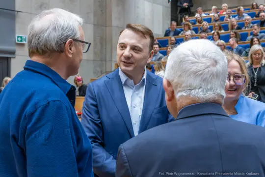Spotkanie grupy ludzi w sali, rozmowy i uśmiechy.