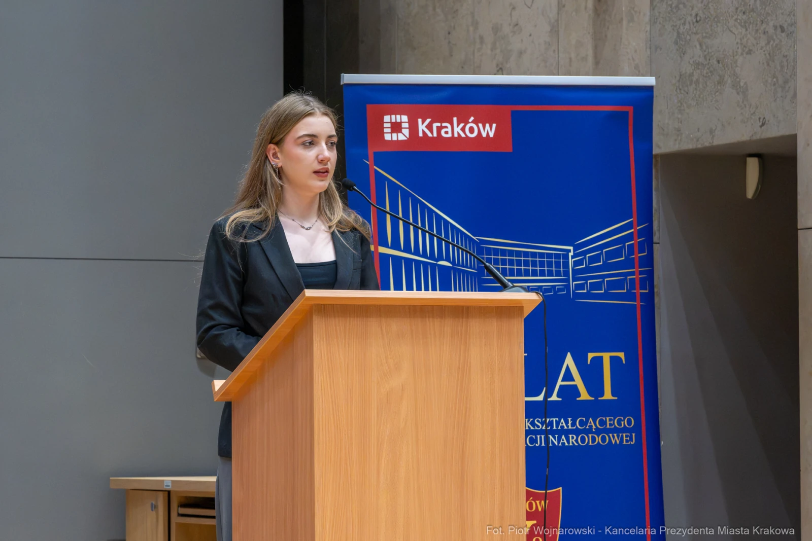 Młoda kobieta przemawia z mównicy, w tle baner z logo Krakowa.  Autor: Piotr Wojnarowski