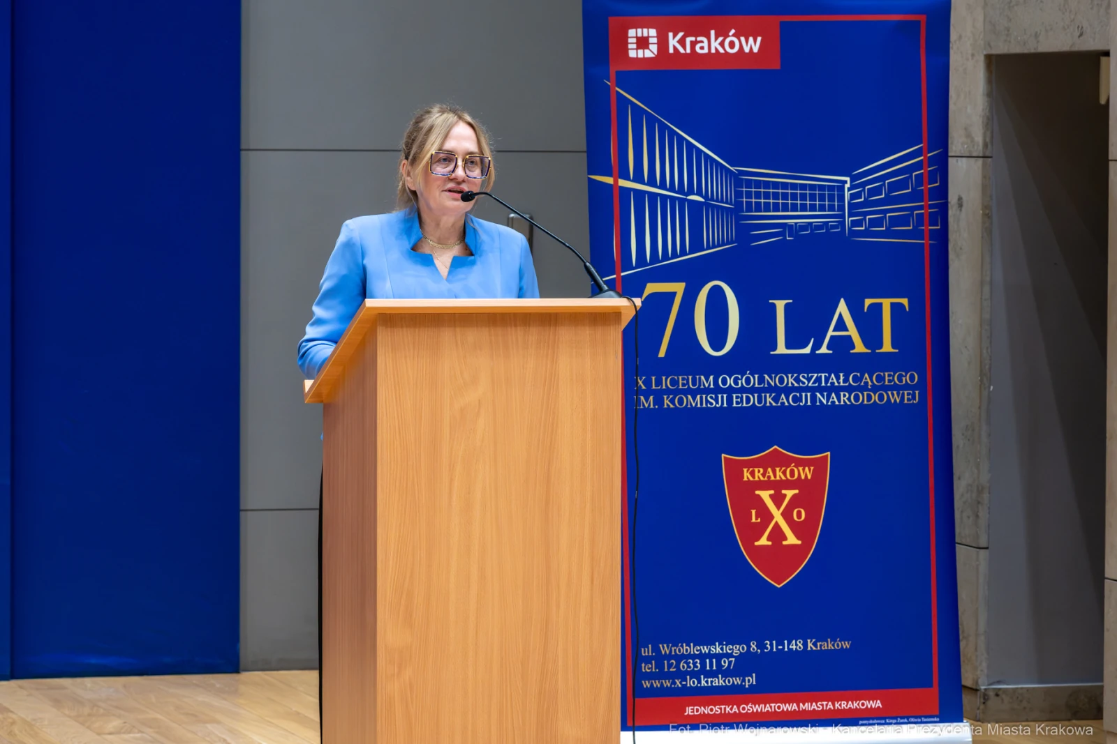 Kobieta przemawia przy mównicy, obok banner z logo szkoły i informacją o 70-leciu.  Autor: Piotr Wojnarowski