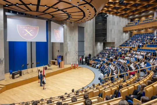 Sala konferencyjna z widownią, na scenie wystąpienie z flagami i logo Krakowa.