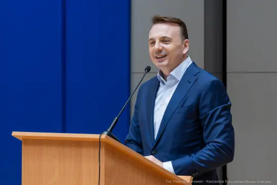 Mężczyzna w garniturze przemawia z uśmiechem przy mównicy.