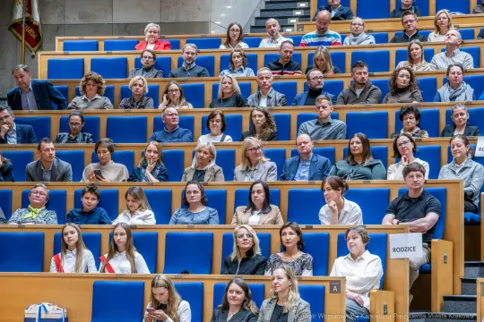 Grupa ludzi siedzących na widowni w sali konferencyjnej.