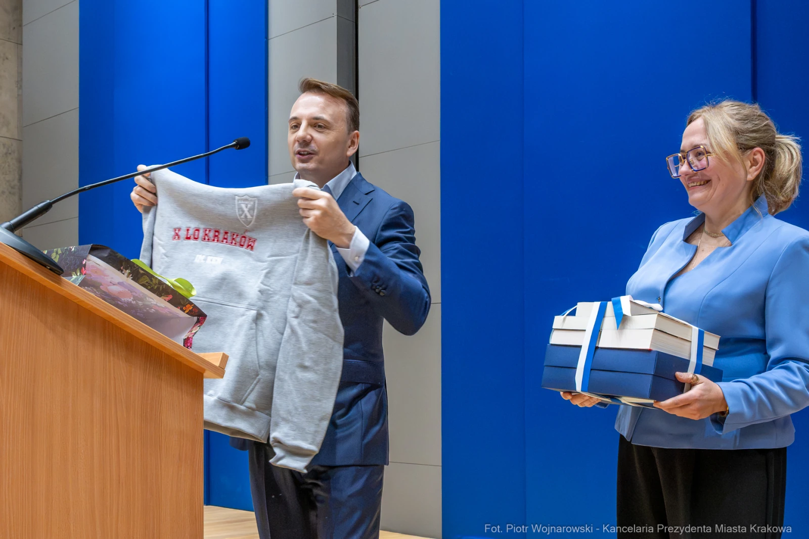 Mężczyzna trzyma szary sweter, kobieta prezentuje niebieskie pudełka.  Autor: Piotr Wojnarowski