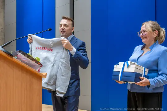 Mężczyzna trzyma szary sweter, kobieta prezentuje niebieskie pudełka.