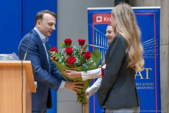 Mężczyzna wręcza bukiet czerwonych róż kobiecie podczas uroczystości.