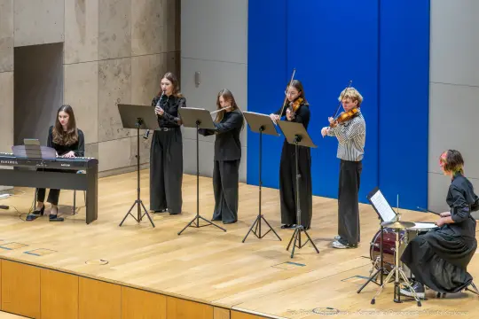 Grupa muzyków grających na różnych instrumentach w sali koncertowej.