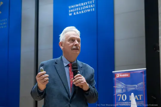 Mężczyzna w garniturze przemawia do publiczności, trzymając w ręku mikrofon.