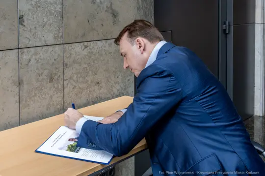 Mężczyzna w garniturze podpisuje dokumenty przy biurku.