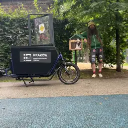 Mężczyzna z długimi włosami stoi obok roweru cargo z napisem Kraków - Miasto Literatury UNESCO.