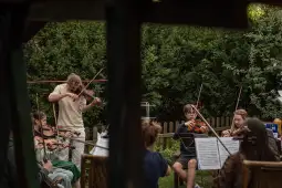 Grupa osób grających na skrzypcach w ogrodzie.