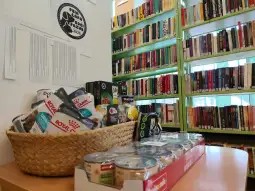 Kosz z jedzeniem i napojami na tle regałów z książkami w bibliotece.