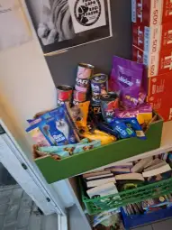 Kosz z różnorodnymi produktami spożywczymi, w tym puszkami i przekąskami.