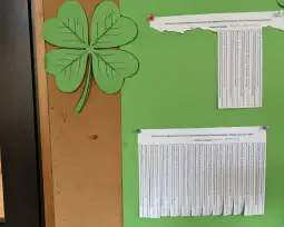 Zielony liść koniczyny na tle korkowej tablicy z tekstem.