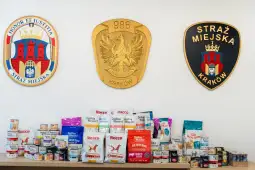 Herby Straży Miejskiej Krakowa oraz różnorodne opakowania karmy dla zwierząt.
